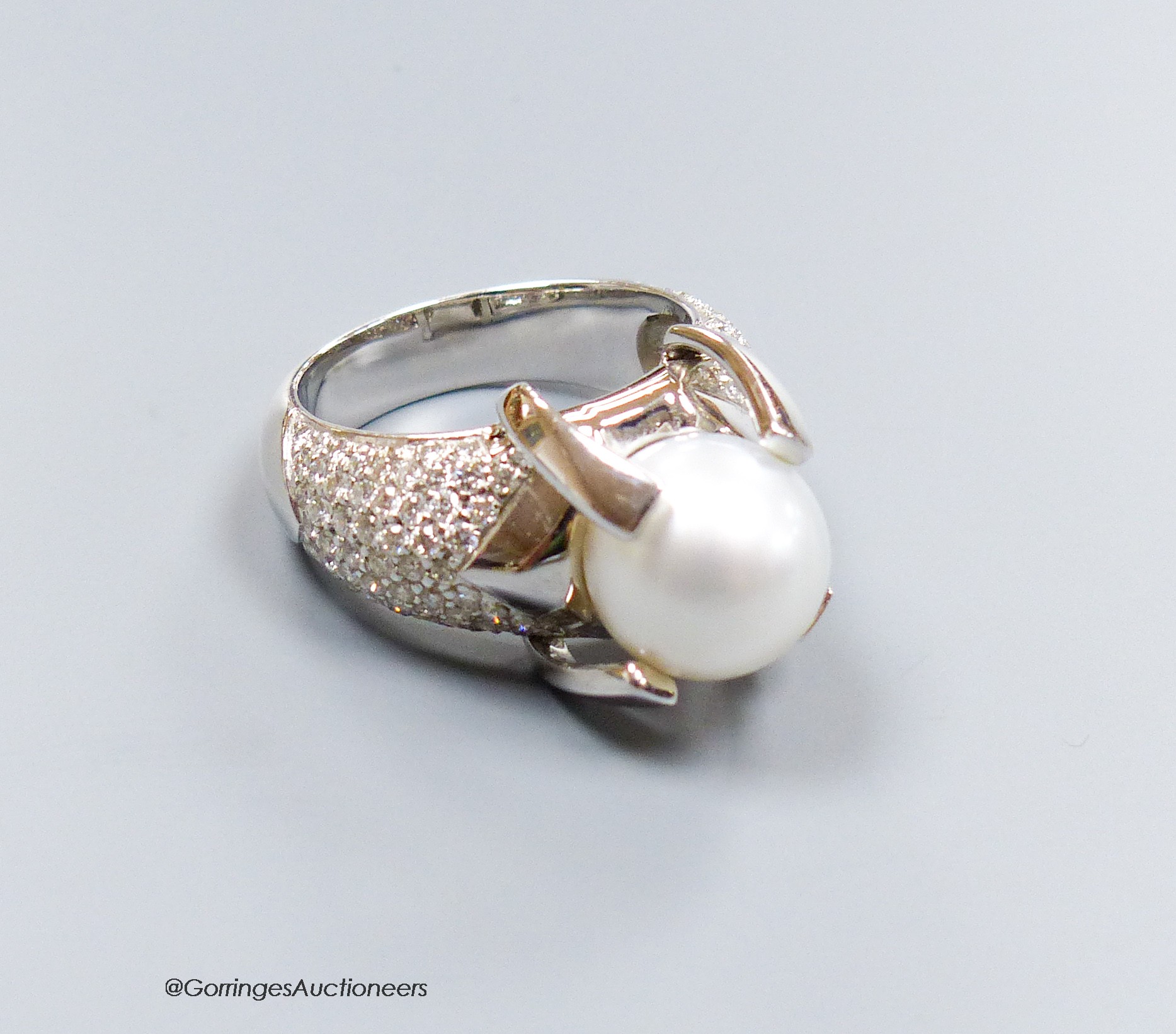 A modern white metal (stamped 750) and claw set cultured pearl dress ring, with pave diamond set shoulders, size R, gross 17.6 grams.